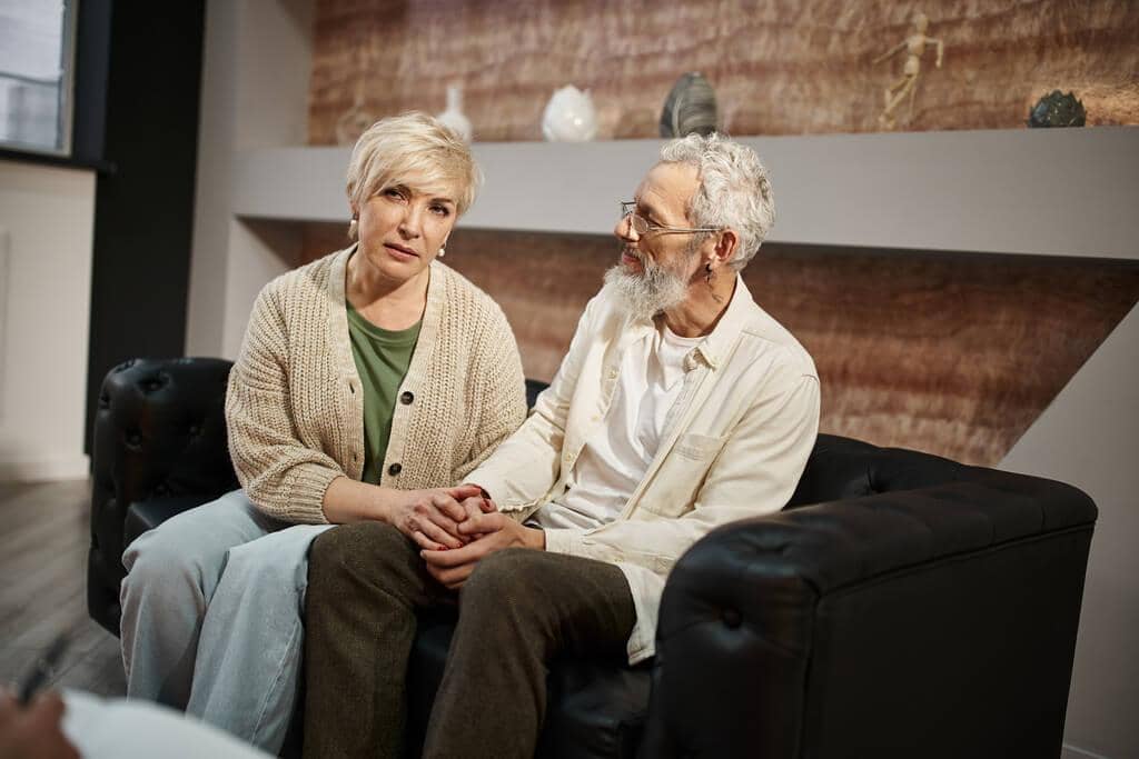 7 Glaring Signs He’s Committed to Misunderstanding You for Control 6 middle aged couple holding hands sitting couch