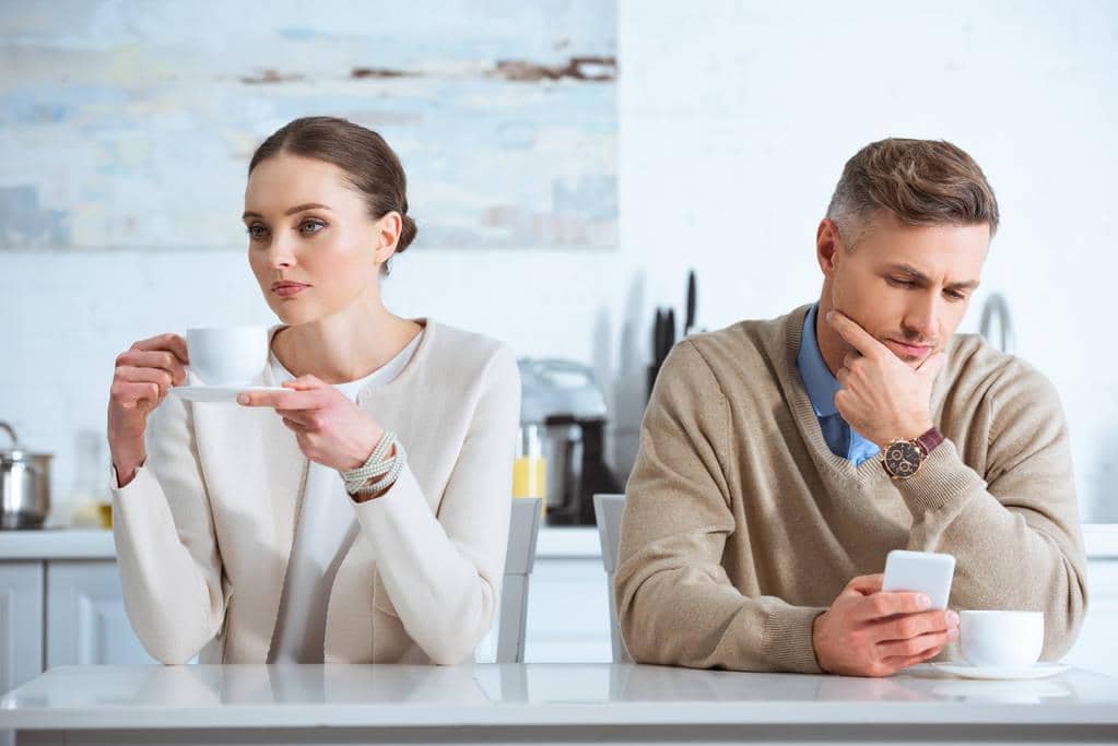 Stonewalling vs Silent Treatment: 9 Big Differences to Know 16 man using smartphone ignoring upset woman breakfast kitchen 1