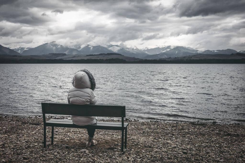 3 Questions Before Leaving a Relationship That Demand Brutal Honesty 2 woman jacket sitting bench shore lake dark cloudy sky mountains 1
