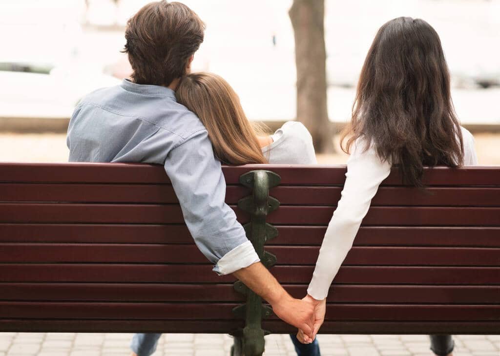 9 Outrageous Lies Men Believe to Justify Infidelity 13 boyfriend holding hands with girlfriends friend sitting on bench outdoor
