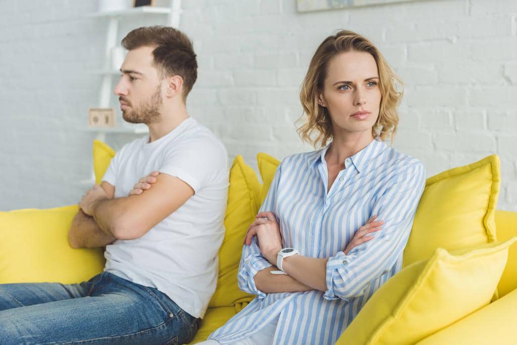50 Painful Signs of an Emotionally Unavailable Husband 2 upset couple sitting yellow couch argue 1