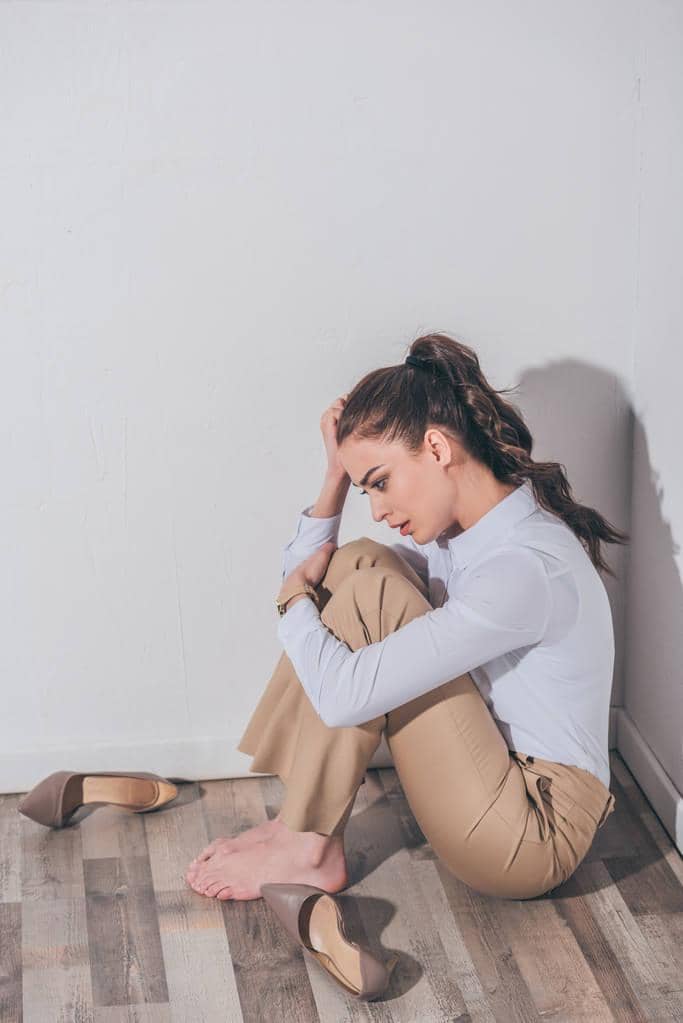 9 Ways Intermittent Reinforcement Keeps You Stuck in Toxic Relationships 3 sad woman white blouse beige pants sitting floor wall home