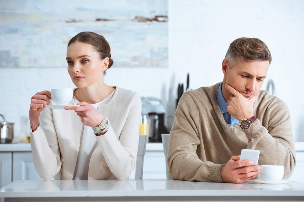 Stonewalling vs Silent Treatment: 9 Big Differences to Know 16 man using smartphone ignoring upset woman breakfast kitchen 1