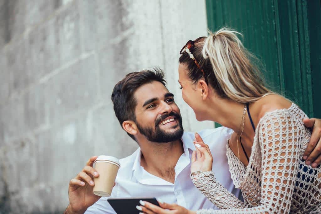romantic tourist couple sitting stairs drinking coffee using digital tablet