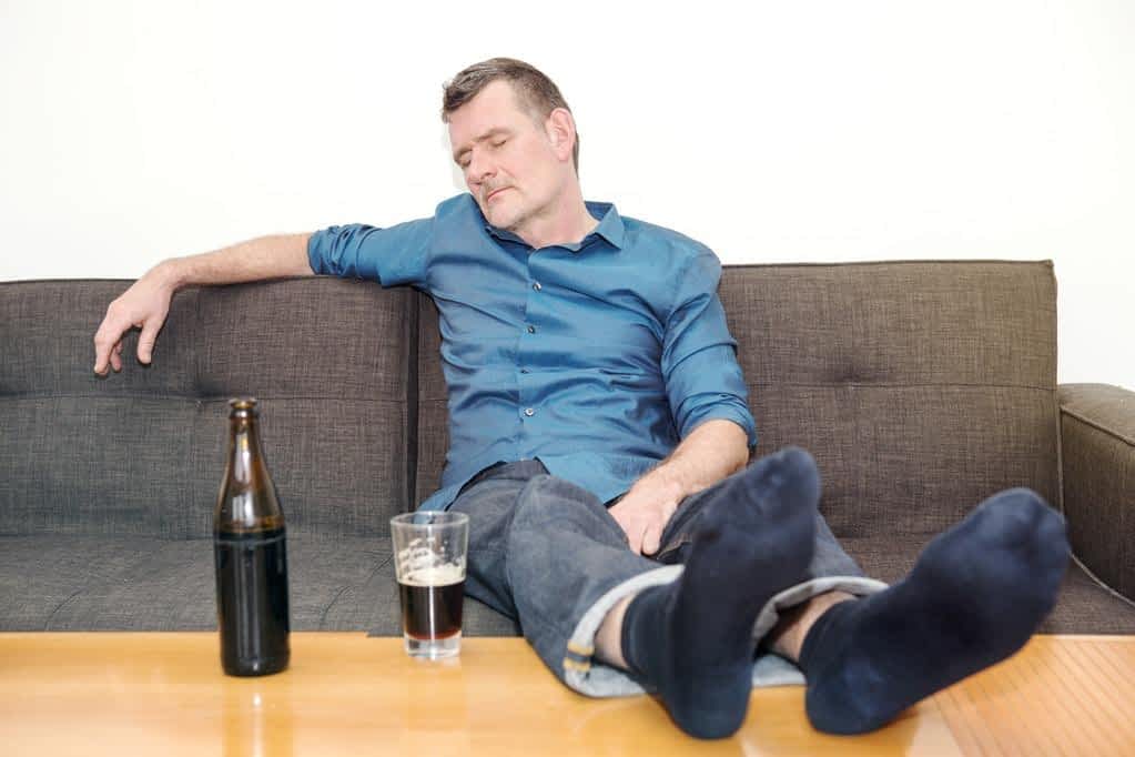 man sleeping on couch with bottle of beer on table
