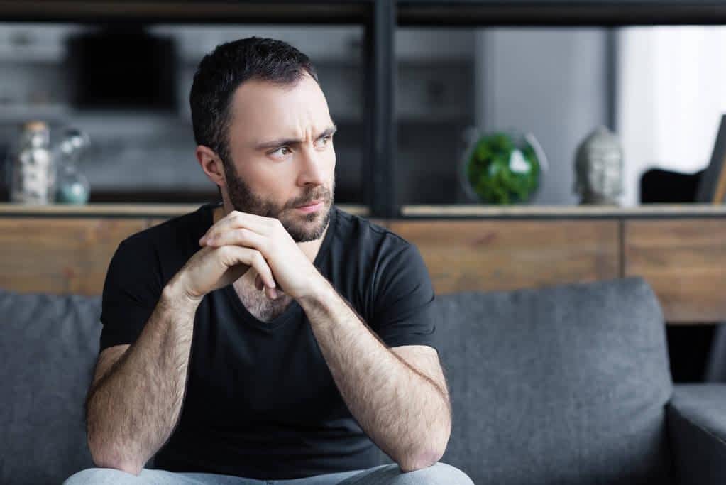 serious bearded man sitting sofa folded hands looking away
