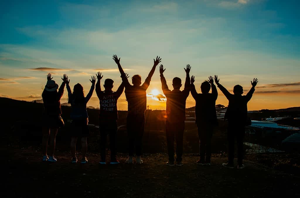 group of guy friends with hands raised at sunest