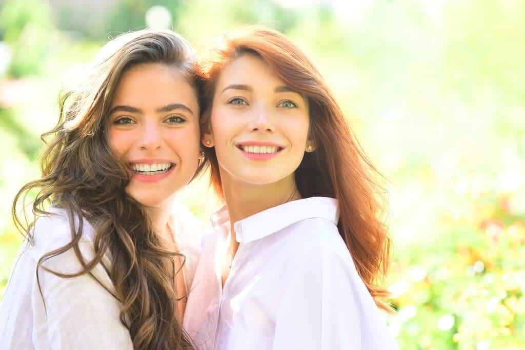 Close up portrait of two beautiful young girls with clear fresh young face skin and perfect nude makeup