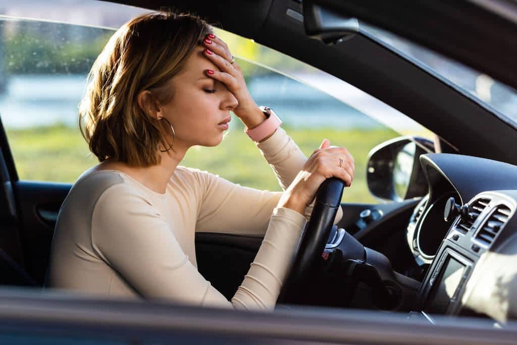 Exhausted woman driver feeling headache, sitting inside her car, keeping hand to head and feeling anxiety.