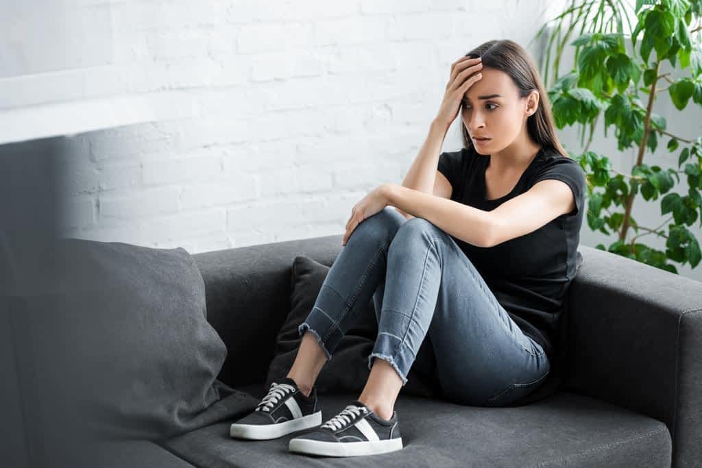 pretty young woman suffering depression while sitting couch home holding
