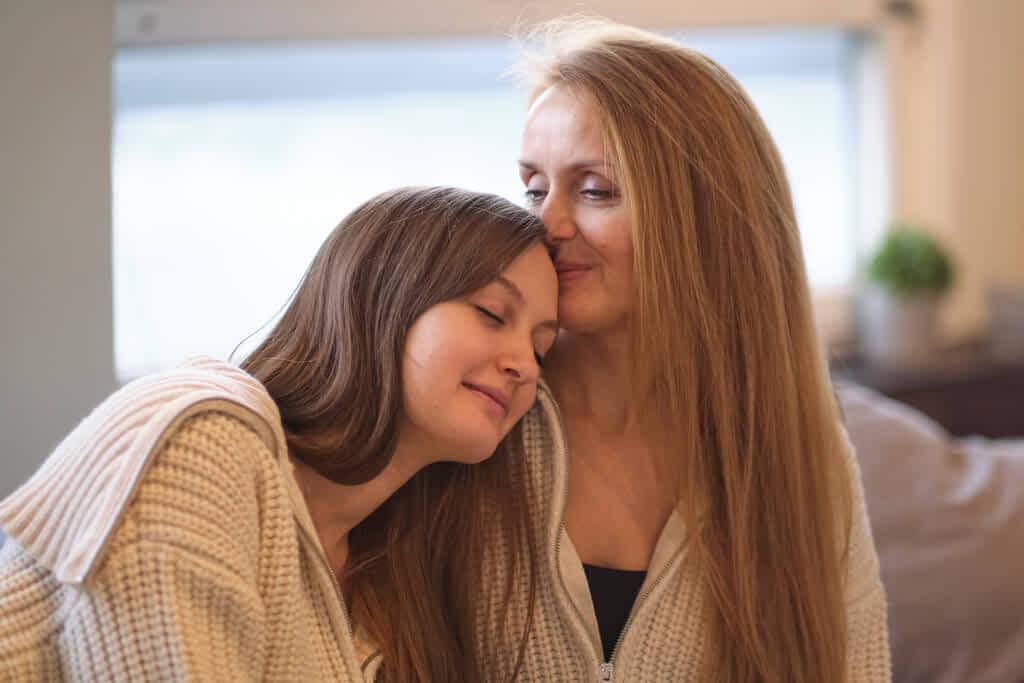 mother and grown up adult daughter sit on couch in living room have fun talking