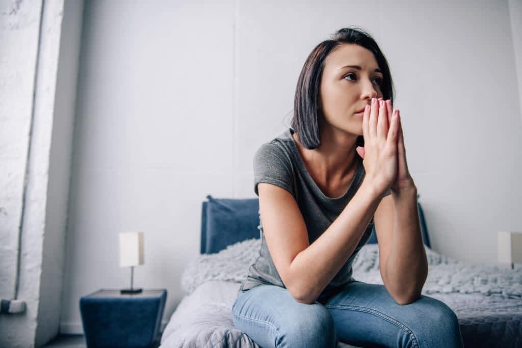 depressed woman sitting bed covering mouth home