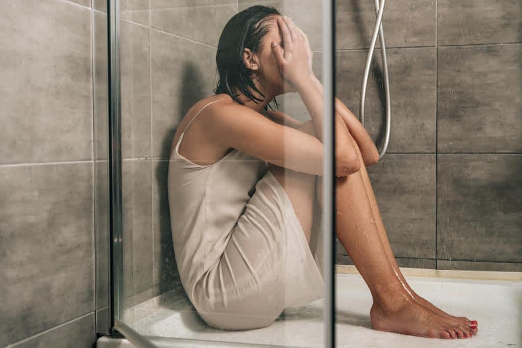 sad depressed woman covering face while sitting shower home