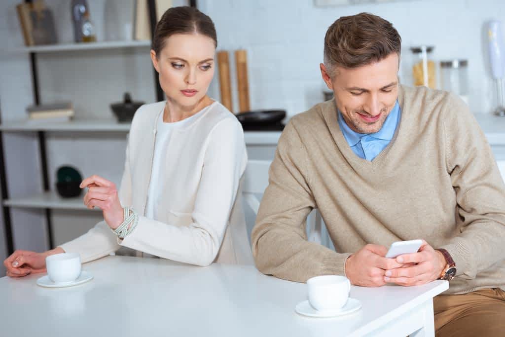 smiling man using smartphone ignoring woman breakfast kitchen