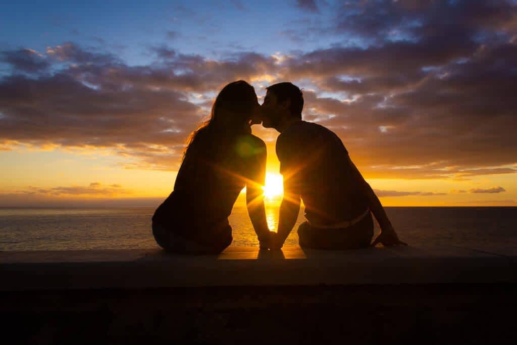 man woman sitting sea kiss sunset