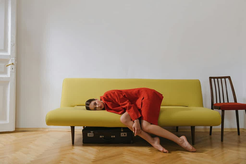 Tired young woman in a red coat lays on the couch with her feet on the floor