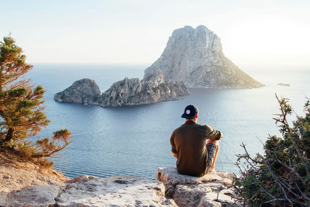 Man sits alone on a rock overlooking the water