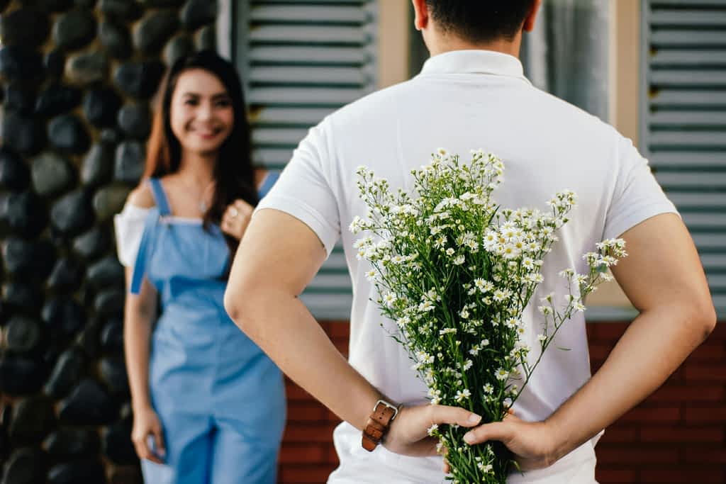 man hides flowers behind his back for his girlfriend