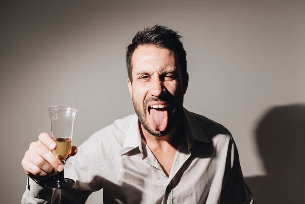 Drunk man sticking tongue out holding an alcoholic drink