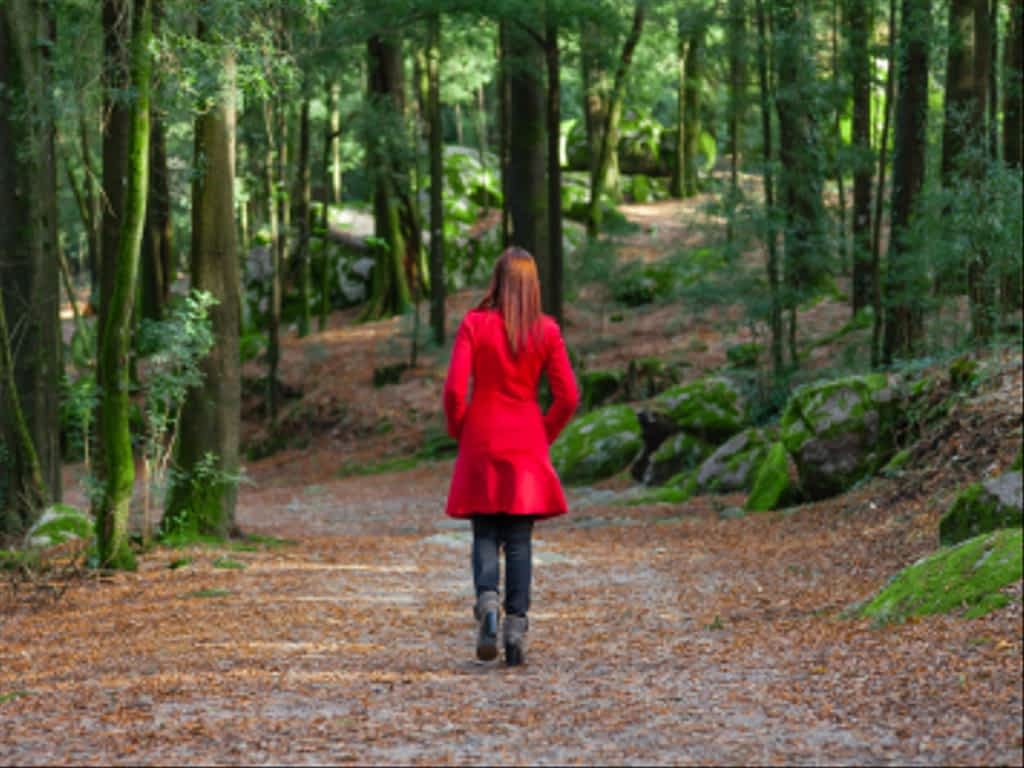 woman walking away alone forest path wearing red long