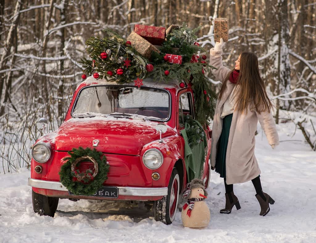 Young woman puts gifts on the roof of an old red car in the snow