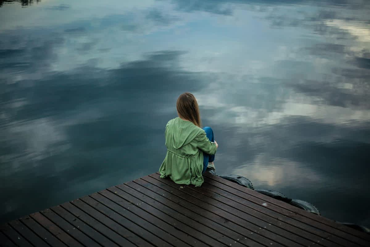 woman sits alone on a pier near the water