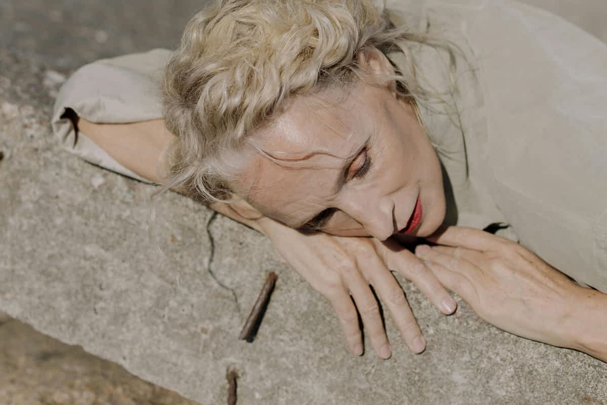 Exhausted, sad woman leans agains a cemet wall with her eyes closed