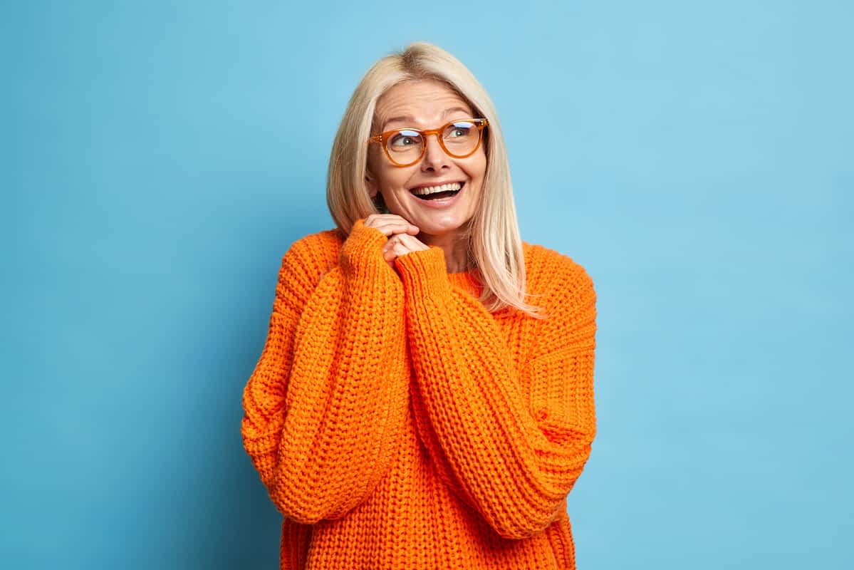 Happy senior woman wearing an orange sweater against a blue background