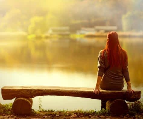 woman sits on a bench by herself near lake at sunset