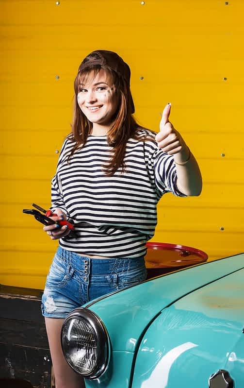 brunette woman in a cap and a striped sweater showing thumb up and holding tools