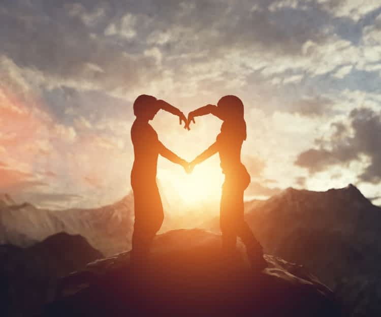 silhouette of couple forming a heart shape with their arms