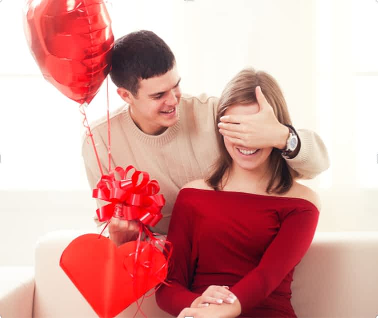 man surprising woman with candy in heart shaped box