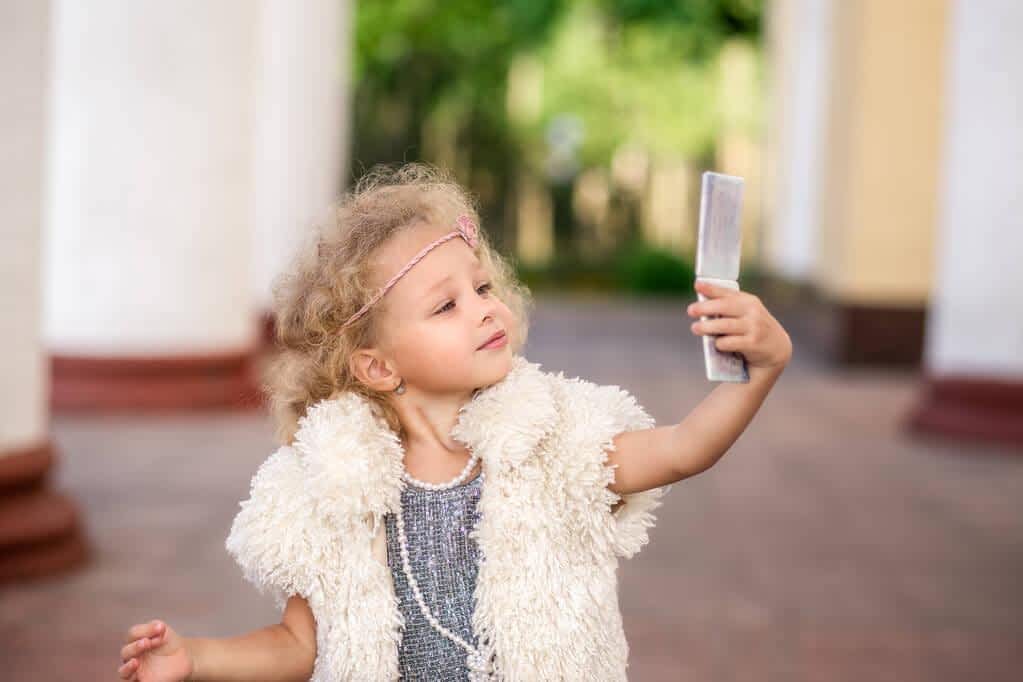 Helicopter Parenting and Narcissism: The Hidden Connection 7 Narcissistic little Girl Admiring herself while taking selfie on phone