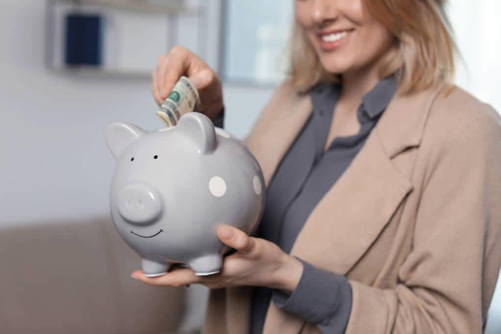 businesswoman putting money into piggy bank indoors closeup
