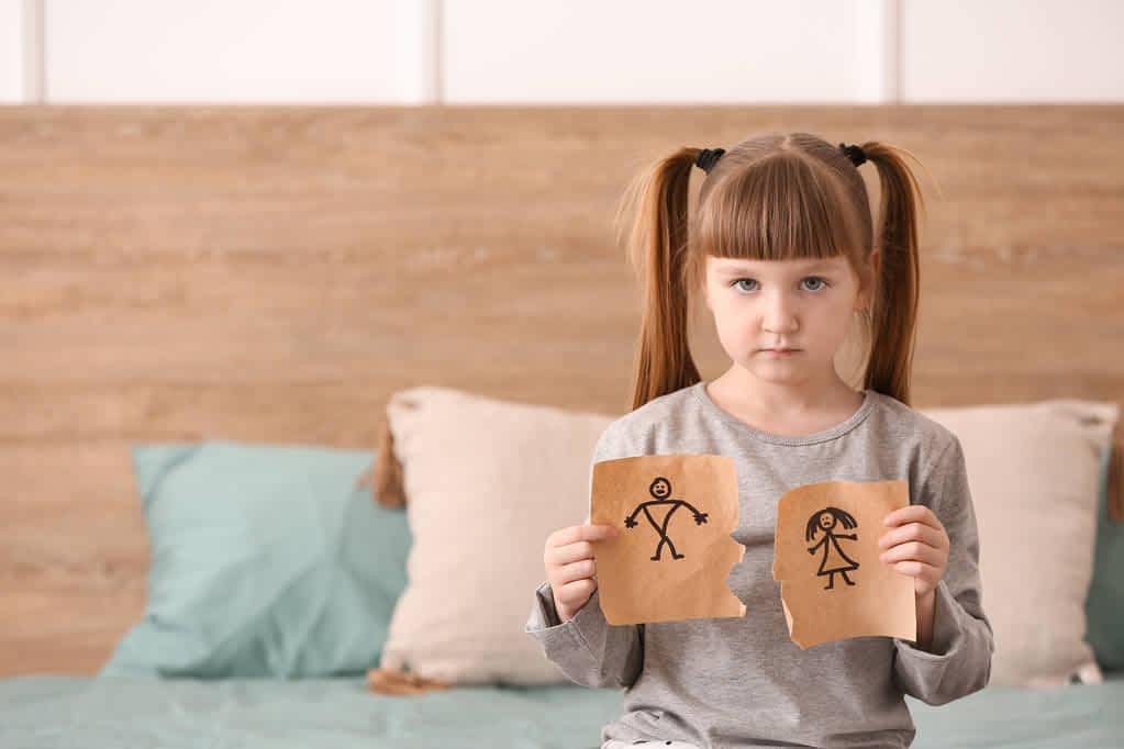 sad little girl with torn drawing of family at home concept of divorce