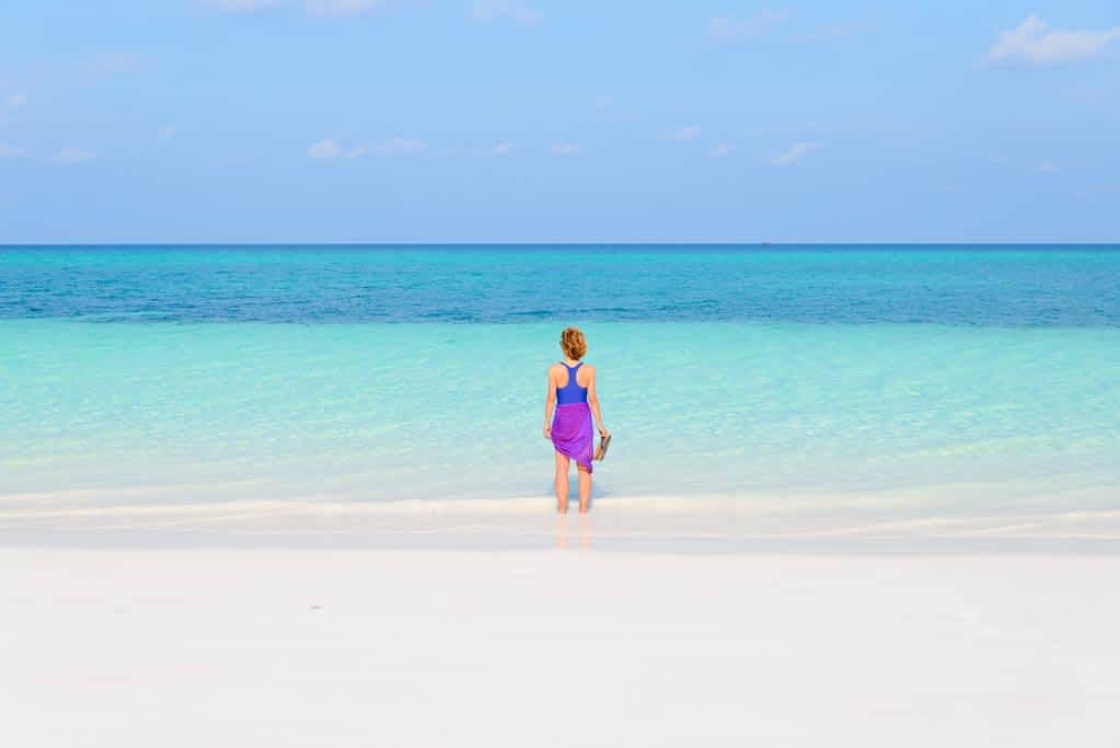 woman walking on tropical beach rear view white sand beach turquoise trasparent water caribbean sea