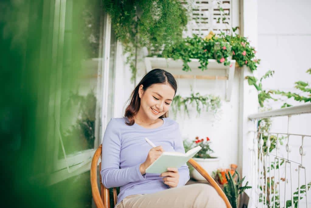woman writing notepad placed white modern chair freelancer home