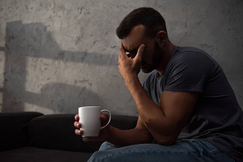 lonely crying man holding cup coffee sitting home