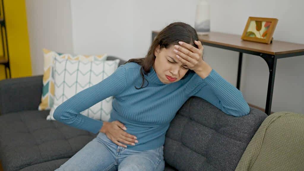 young beautiful hispanic woman suffering menstrual pain sitting sofa home