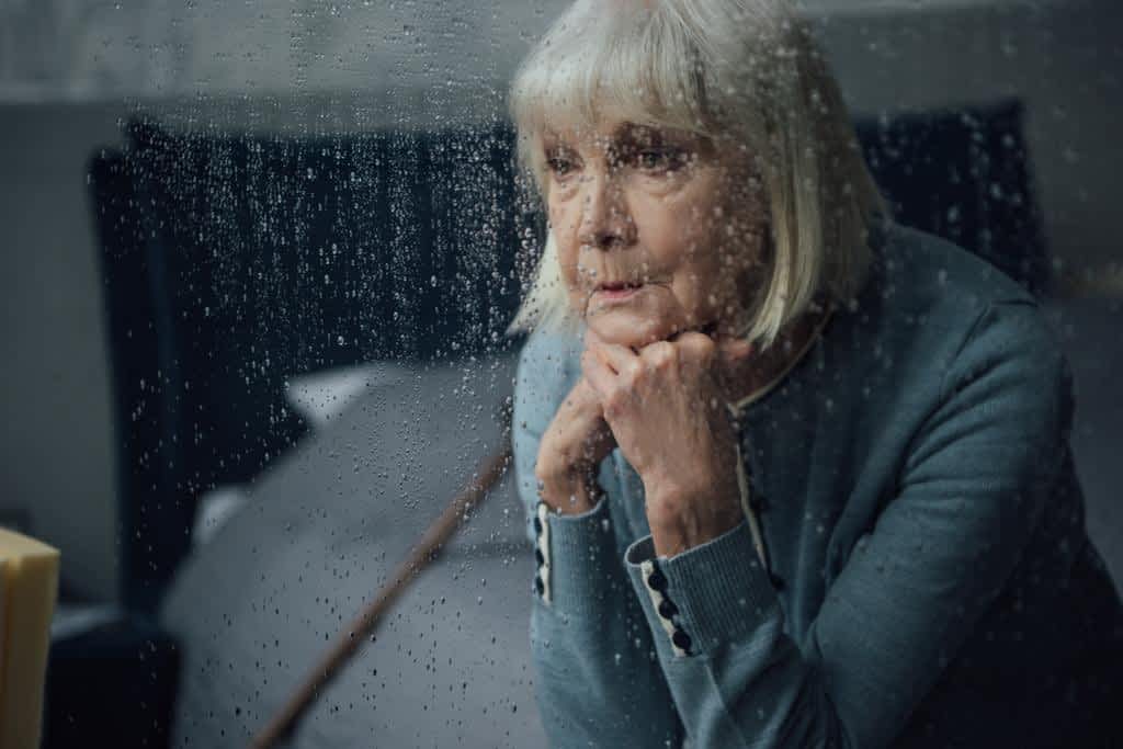 7 Emotional Pitfalls You Need to Avoid During Gray Divorce 2 upset senior woman sitting propping chin hands home window raindrops