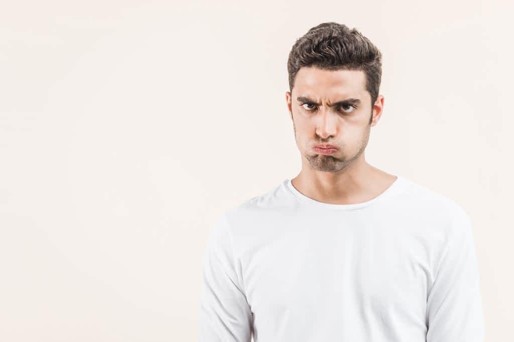 Male Fragility and Abusive Relationships: The Psychological Underpinnings 6 angry young man blowing cheeks looking camera isolated beige