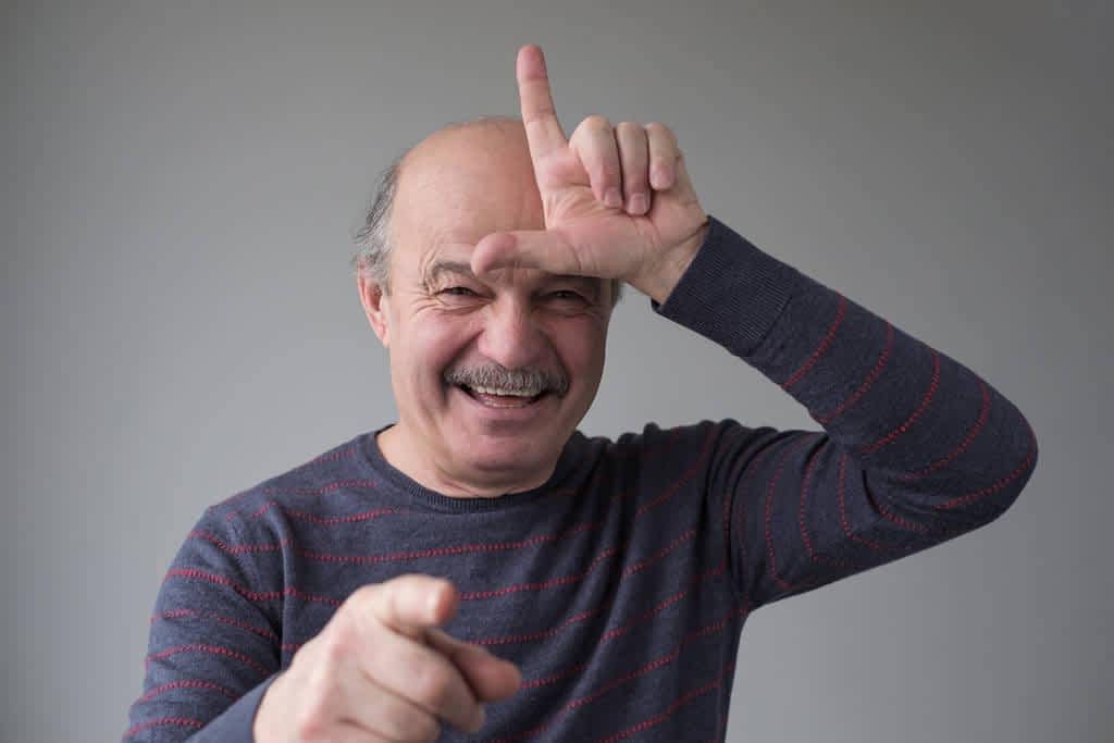 man showing sign over forehead and smiling broadly bragging about victory
