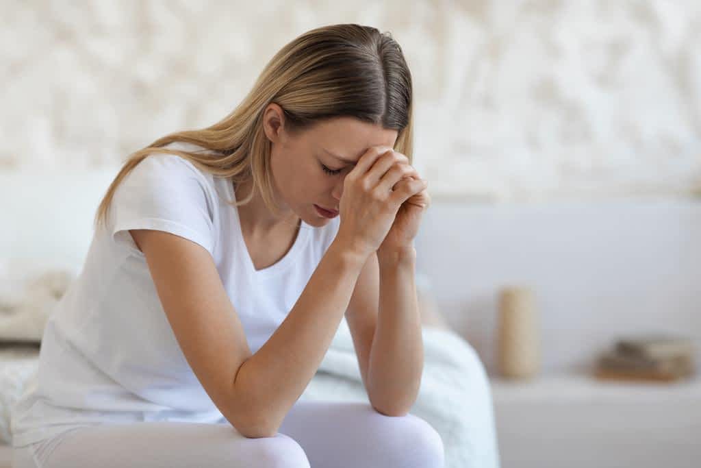 upset blonde lady sitting on bed at home crying