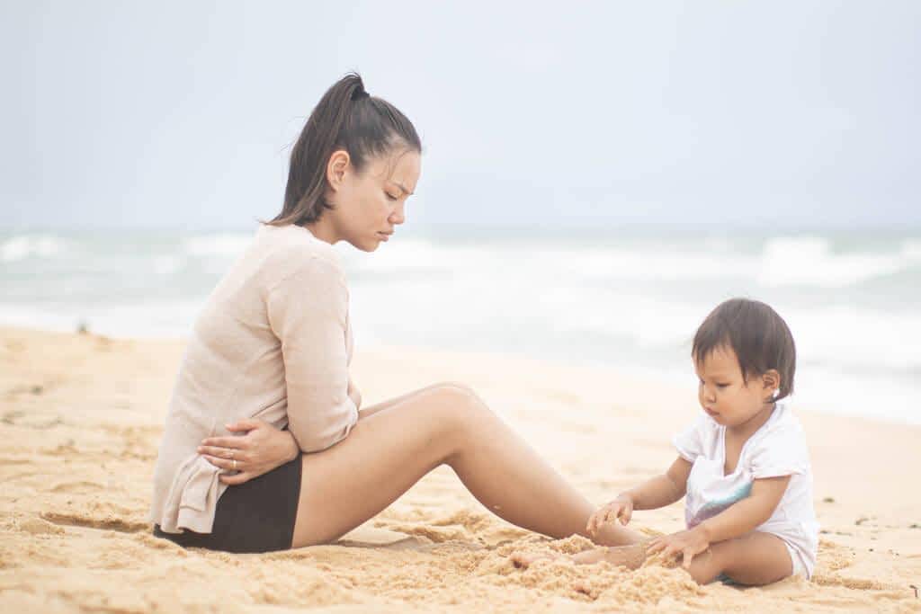 an upset woman looks at her baby play in the sand