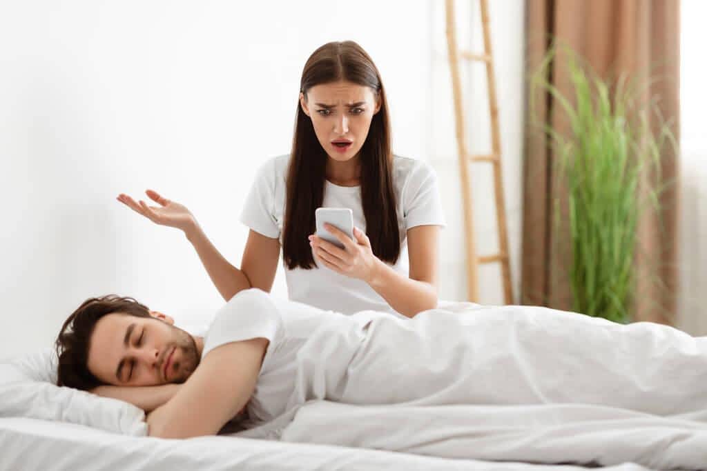 girlfriend holding cheating boyfriends phone reading his messages in bedroom