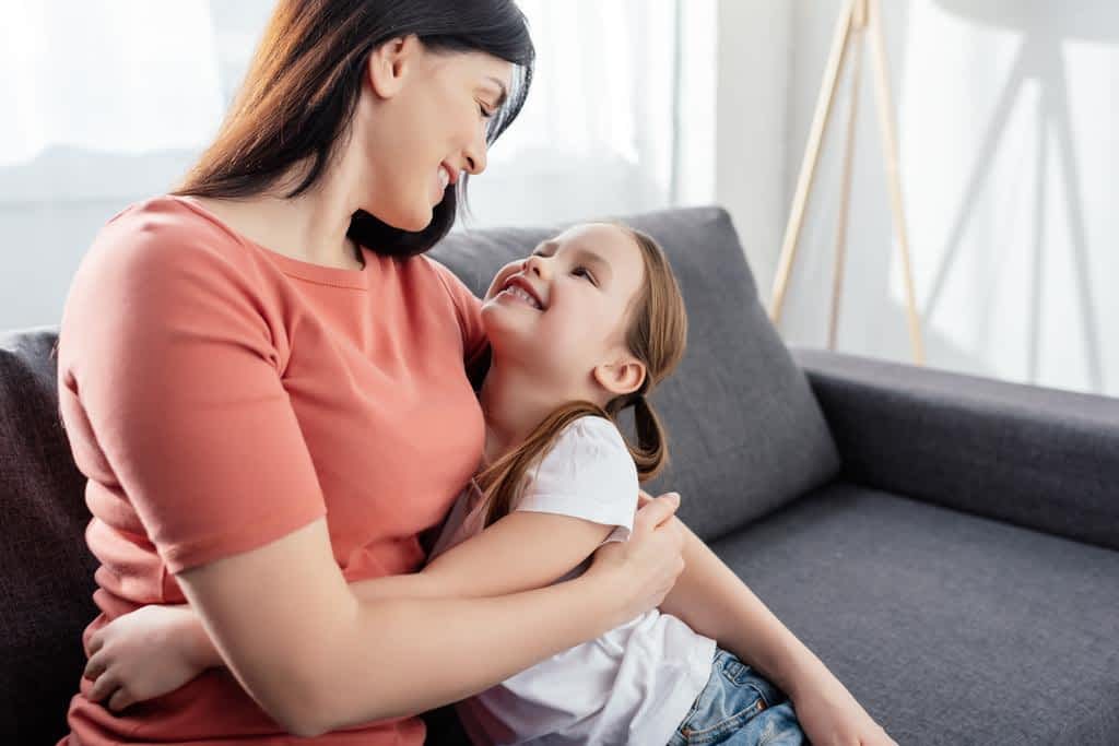 smiling kid embracing looking mother while sitting couch living room