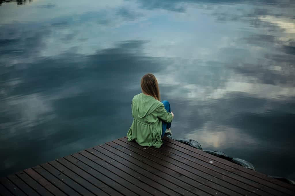 The Exact Moment Most Couples Give Up, According to Marriage Therapists 2 woman sits alone on a pier near the water