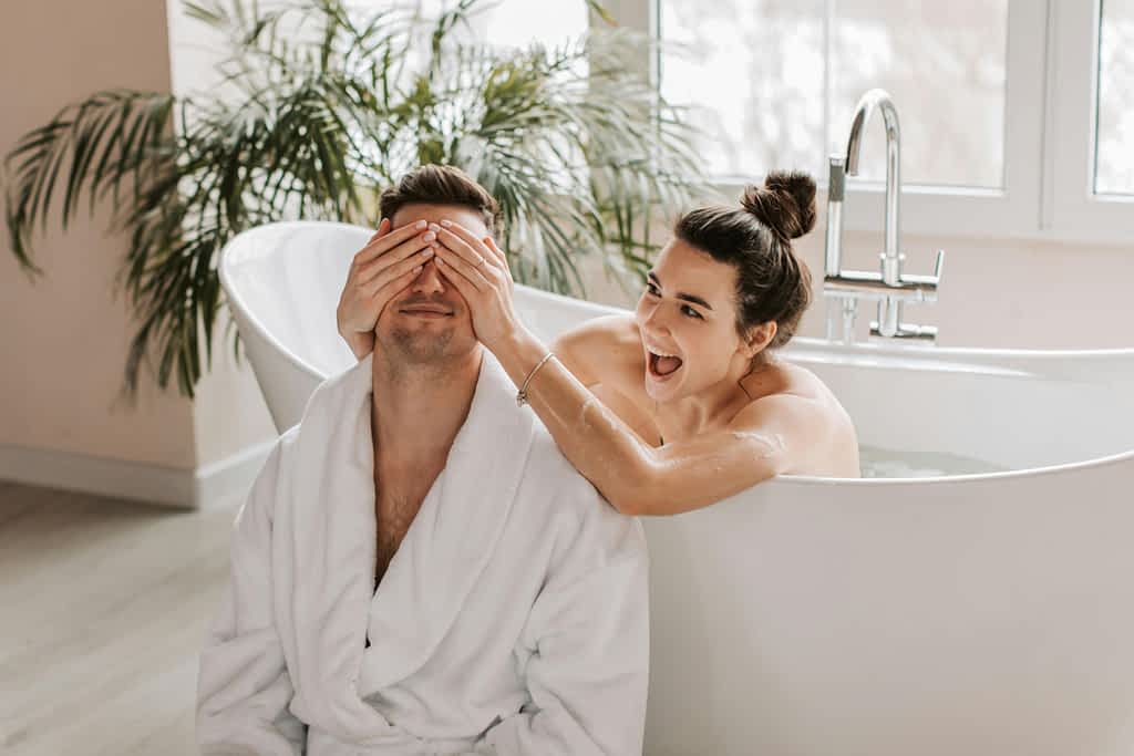 How I Finally Got My Husband to Shower Without Starting World War III 2 woman in bath tub with her hands over husbands eyes