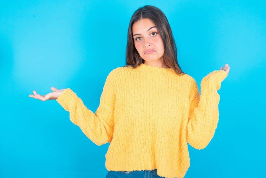 How Indifference in Relationships Can Ruin, or Save It 9 attractive young brunette woman wearing yellow sweater blue background shrugging