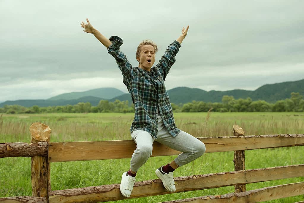 woman sitting on a wood fence looking victorious